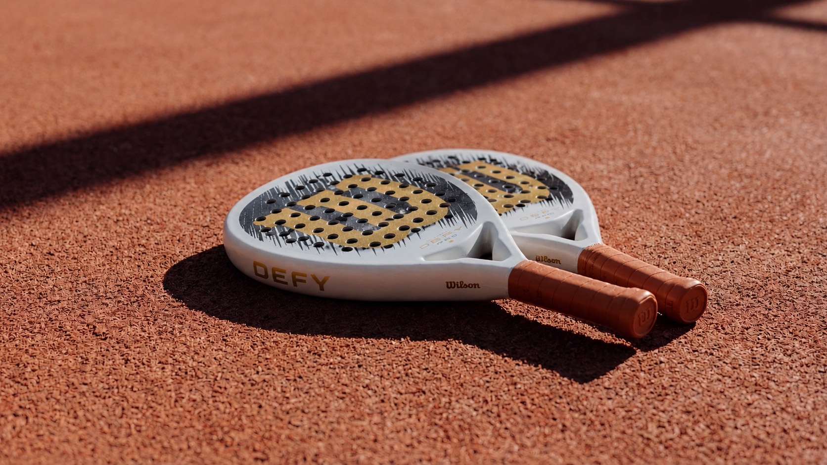 Two Wilson DEFY rackets resting on a sunlit terracotta court.